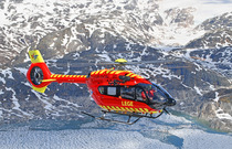 Rødt helikopter fra Norsk Luftambulanse som flyr over fjell